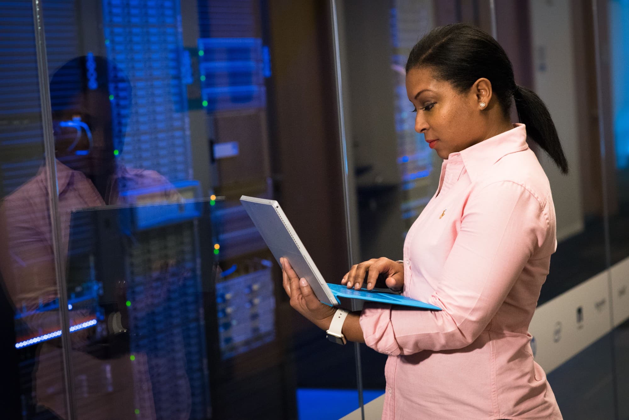 A data center engineer in a pink shirt checking a laptop beside a row of server racks