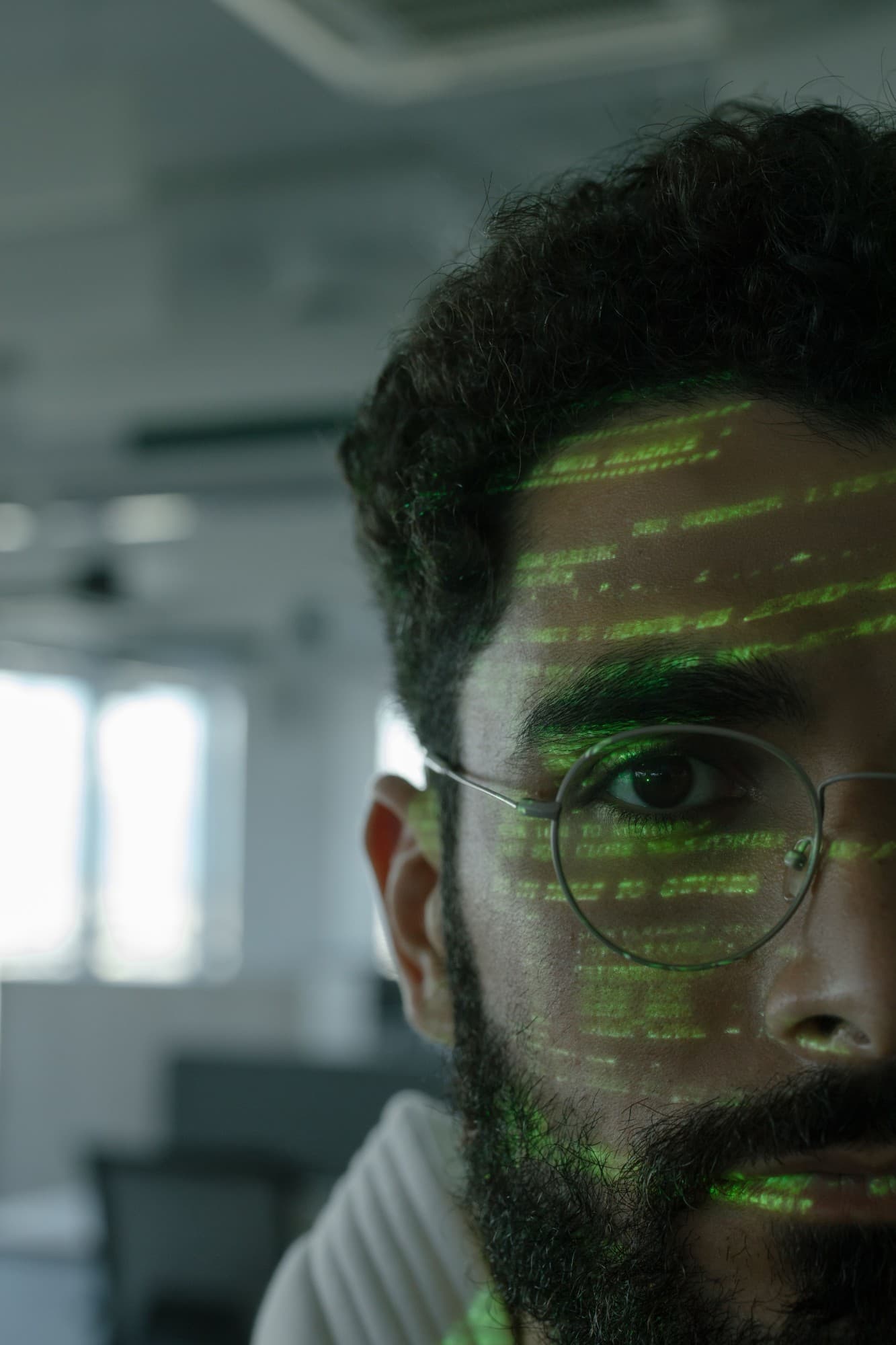Close-up of an engineer in round glasses with lines of green code projected across their face